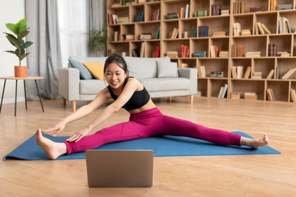 Домашні відео тренування. Спортивна азіатська леді в спортивному одязі тягнеться на йога мат під час перегляду онлайн-підручник на ноутбуці — стокове фото
