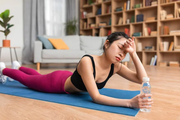 Exhausted asian lady wiping sweat from her forehead, feeling tired after training at home, lying on yoga mat — Foto Stock
