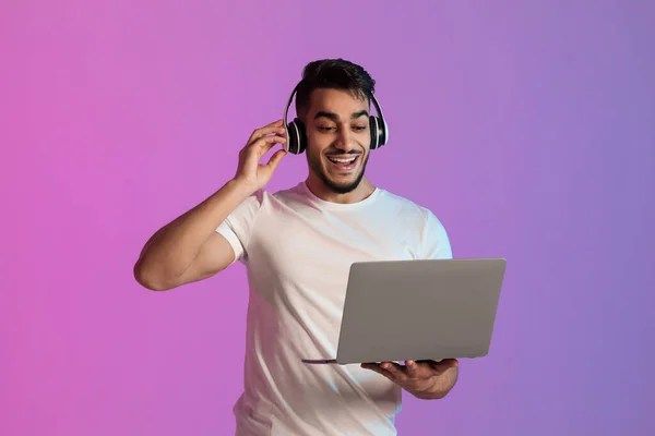 Nadšený Arab nosí sluchátka, dívá se na obrazovku notebooku, nadšený z obrovského prodeje ve webovém obchodě v neonovém světle — Stock fotografie