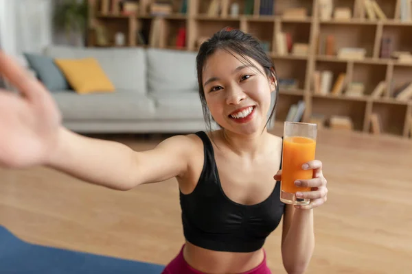 Healthy lifestyle concept. Fit asian lady making selfie with fresh juice, enjoying healthy drink, sitting on yoga mat — ストック写真