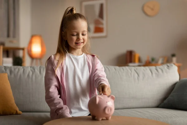 Niña poniendo dinero en Piggybank invirtiendo dinero en casa — Foto de Stock