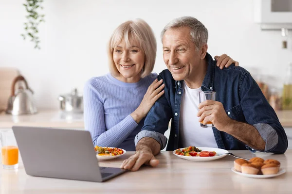 Gelukkig senior paar met behulp van computer tijdens het ontbijt — Stockfoto