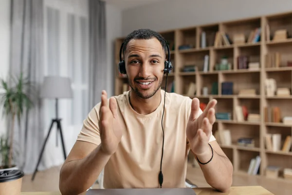 Positive arab freelancer guy in headphones having online video call, speaking to business partner and gesturing at camera — Fotografia de Stock