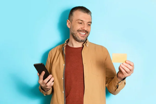 Vrolijke man met een creditcard en telefoon over blauwe achtergrond — Stockfoto