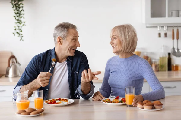 Happy elderly man and woman having lunch at home, chatting — Stockfoto