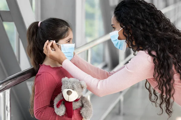 Cuidar a mamá joven con máscara médica protectora para su hija en el aeropuerto —  Fotos de Stock