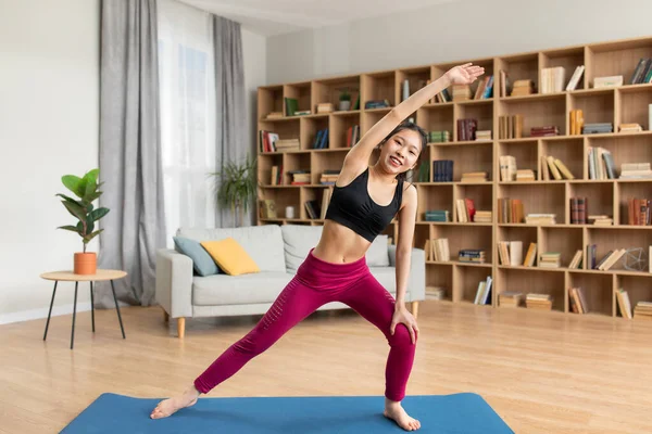 Slim asian lady stretching her body on yoga mat during her home workout,  looking and smiling at camera - Stock Image - Everypixel