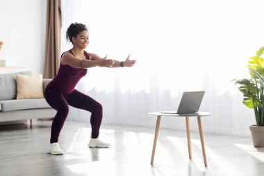 Attractive black woman training at home, having online fitness class