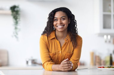 Mutfak masasında oturan güzel Afro-Amerikan kadının portresi.