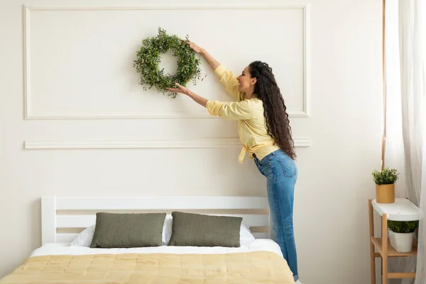 Pretty young smiling lady putting decor on wall — Stockfoto