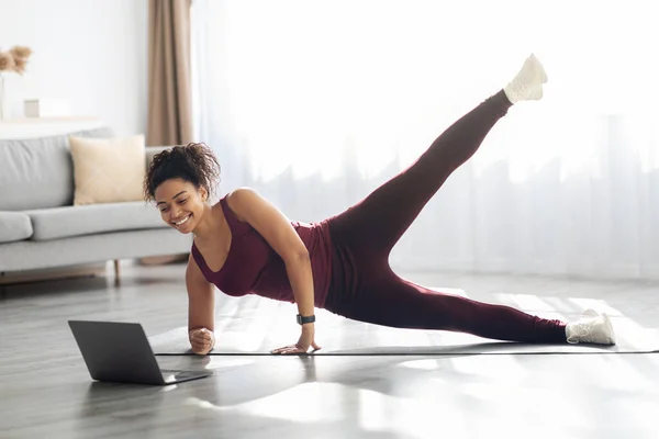 Sporty african american woman exercising at home, using laptop — Stockfoto