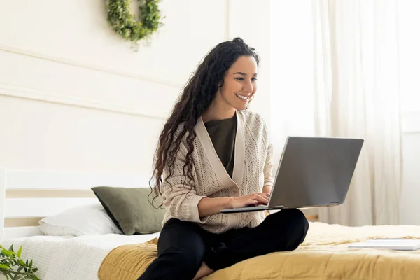 Wanita tersenyum menggunakan laptop berbaring di tempat tidur di rumah — Stok Foto