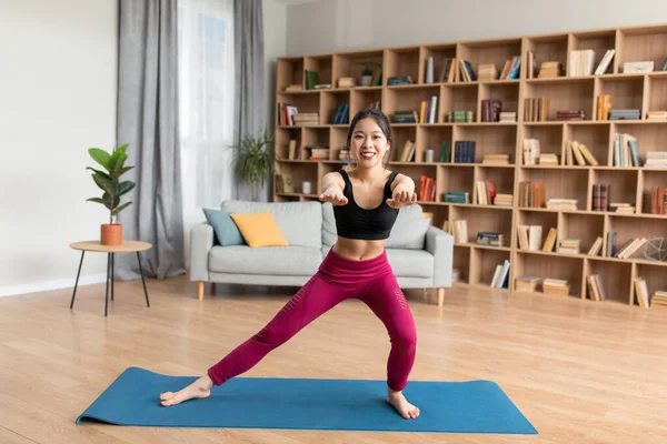 Genç Koreli kadın hamleler yapıyor, evde yoga minderi üzerinde egzersiz yapıyor, gücünü geliştiriyor, uzayı kopyalıyor.