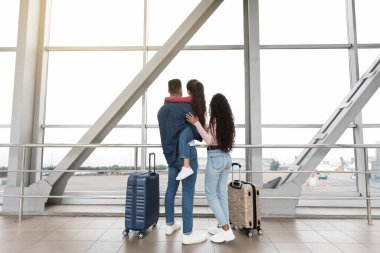 Family Trip. Parents With Daughter Standing Near Window At Airport, Rear View