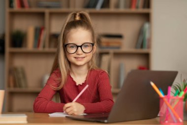 Smiling Little Schoolgirl Posing Near Laptop Taking Notes At Home