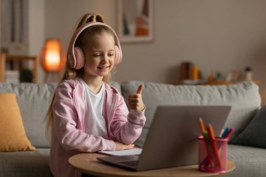 Küçük liseli kız dizüstü bilgisayar kullanıyor. Parmak uçlarını kaldırarak evde oturuyor.