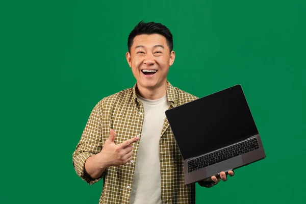Новий сайт. Захоплений зрілий азіатський чоловік тримає ноутбук з порожнім екраном і вказує на монітор, макет — стокове фото