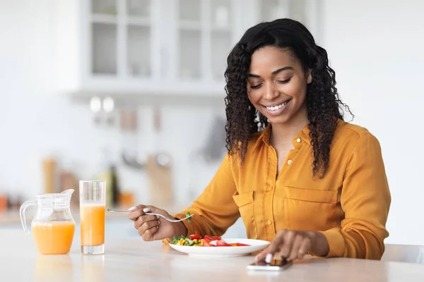 Sorridente donna nera che naviga sui social media mentre fa colazione — Foto Stock