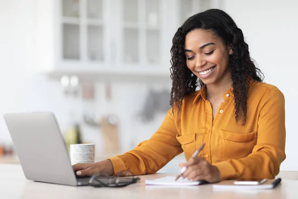 Cheerful pretty black lady working from home, taking notes — Photo