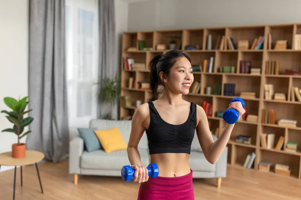 Slim young korean woman lifting up dumbbells having training at home, taking care of body in the morning — Stockfoto