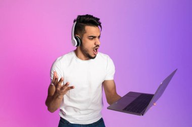 Kulaklıklı öfkeli genç bir Arap dizüstü bilgisayara bağırıyor, hayal kırıklığına uğramış hissediyor, son teslim tarihini kaçırıyor