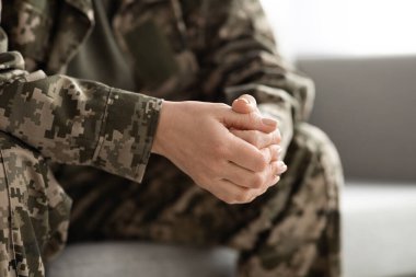 Unrecognizable Female In Camouflage Uniform Sitting On Couch With Clasped Hands