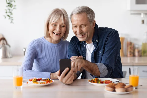 Kahvaltı yaparken akıllı telefon kullanan mutlu yaşlı çift. — Stok fotoğraf