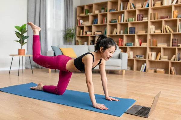Domestic body shaping and glutes workout. Asian lady training butts on yoga mat, looking at laptop screen — Stockfoto