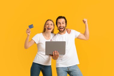 Satisfied excited millennial caucasian husband and wife in white t-shirts showing victory gesture and hold credit card