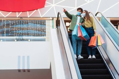 Couple Shopping Wearing Masks Standing On Moving Stairs In Mall