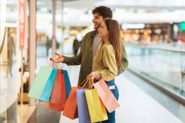 Happy Couple Shopping Standing Near Shop Window In Mall