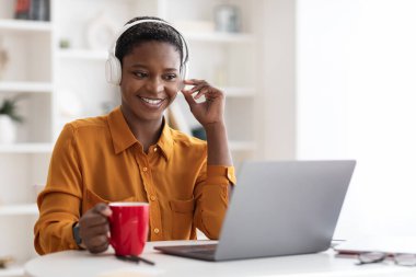 Genç siyahi kadın iş arkadaşlarıyla video konferansı yapıyor, kahve içiyor.
