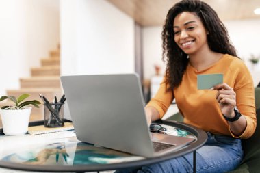 Happy black woman holding debit credit card, using computer