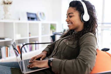 Smiling black woman in headset using laptop at home