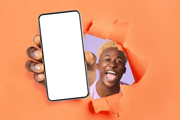 Happy excited young african american guy winner with open mouth looks through hole in orange paper — Φωτογραφία Αρχείου