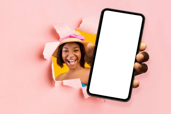 Cheerful excited millennial african american woman with open mouth in hat looks through hole in pink paper — Stockfoto