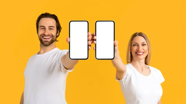 Gülümseyen genç Avrupalı kadın ve beyaz tişörtlü adam akıllı telefonları sunuyor. — Stok fotoğraf