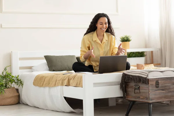 Kvinna med bärbar dator gör videosamtal sitter på sängen — Stockfoto