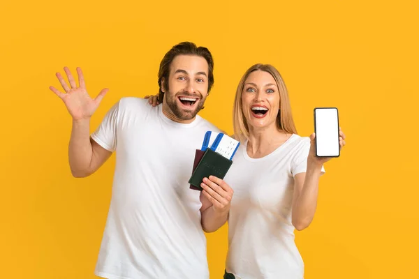 Satisfied excited young european couple showing smartphone with empty screen and passports with air tickets — стокове фото