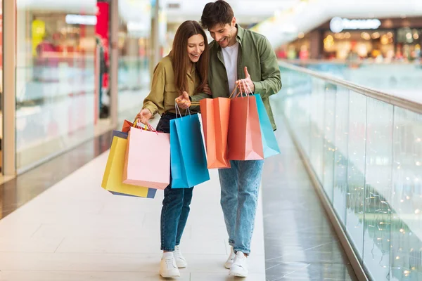 Excited Couple Looking Into Shopping Bags Standing In Modern Mall — Zdjęcie stockowe