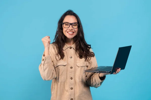 Ευτυχισμένη νεαρή Ευρωπαία μελαχρινή μαθήτρια με γυαλιά χαίρεται για τη νίκη και την επιτυχία συμφωνία, κρατήστε το laptop — Φωτογραφία Αρχείου