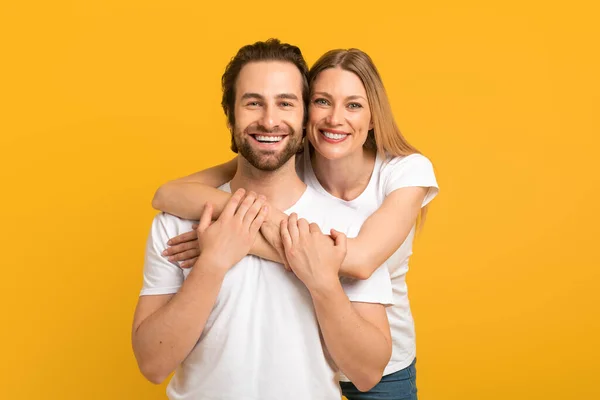 Alegre milenario europeo hembra abrazándose desde atrás macho con rastrojo en blanco camisetas mirando a la cámara — Foto de Stock