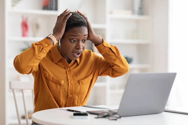 Shocked african american woman with earpods looking at laptop screen — стокове фото