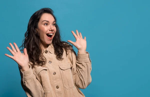 Happy surprised excited young european brunette woman in casual with raised hands looking to empty space - Stock-foto