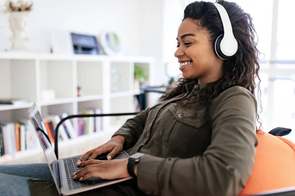 Leende svart kvinna i headset med bärbar dator hemma — Stockfoto