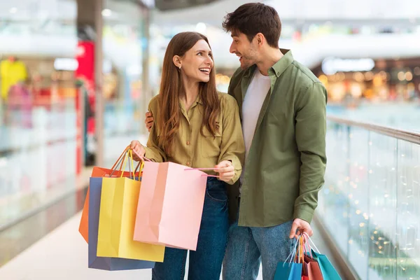 Radosna para robi zakupy trzymając kolorowe torby Shopper w centrum handlowym — Zdjęcie stockowe