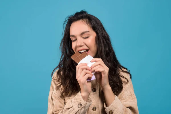 Happy young european brunette woman with closed eyes eats chocolate and enjoys taste of sweets — Stok fotoğraf