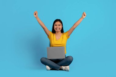 Gündelik giyinmiş genç Çinli bayanın dizüstü bilgisayarla yere oturup zaferle el kaldırmasına sevindim.