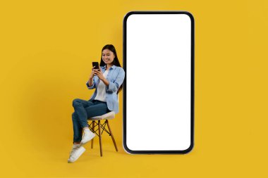 Sıradan giyinen Koreli genç bayanın sandalyeye oturup akıllı telefondan blog okumasına sevindim.