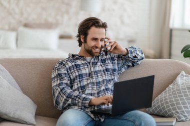 Milenyum boyunca sakallı beyaz erkek koltukta oturur telefonda konuşur ve oturma odasında dizüstü bilgisayara bakar.